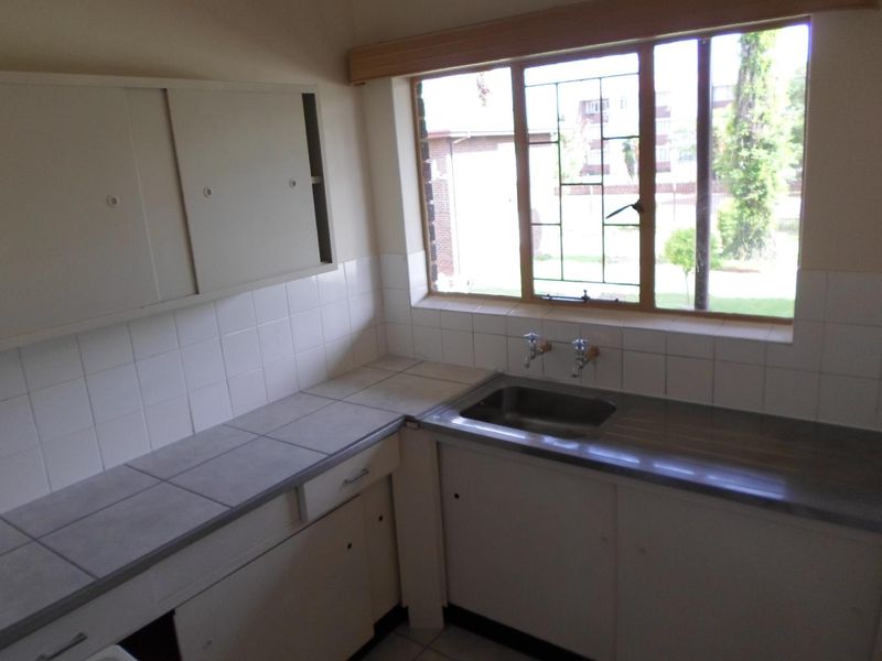 A dated kitchen featuring tiled countertops, a stainless steel sink, and original cabinetry, offering a blank canvas for a modern renovation.