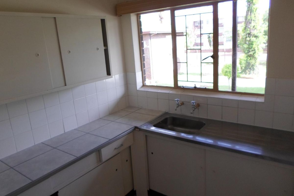 A dated kitchen featuring tiled countertops, a stainless steel sink, and original cabinetry, offering a blank canvas for a modern renovation.