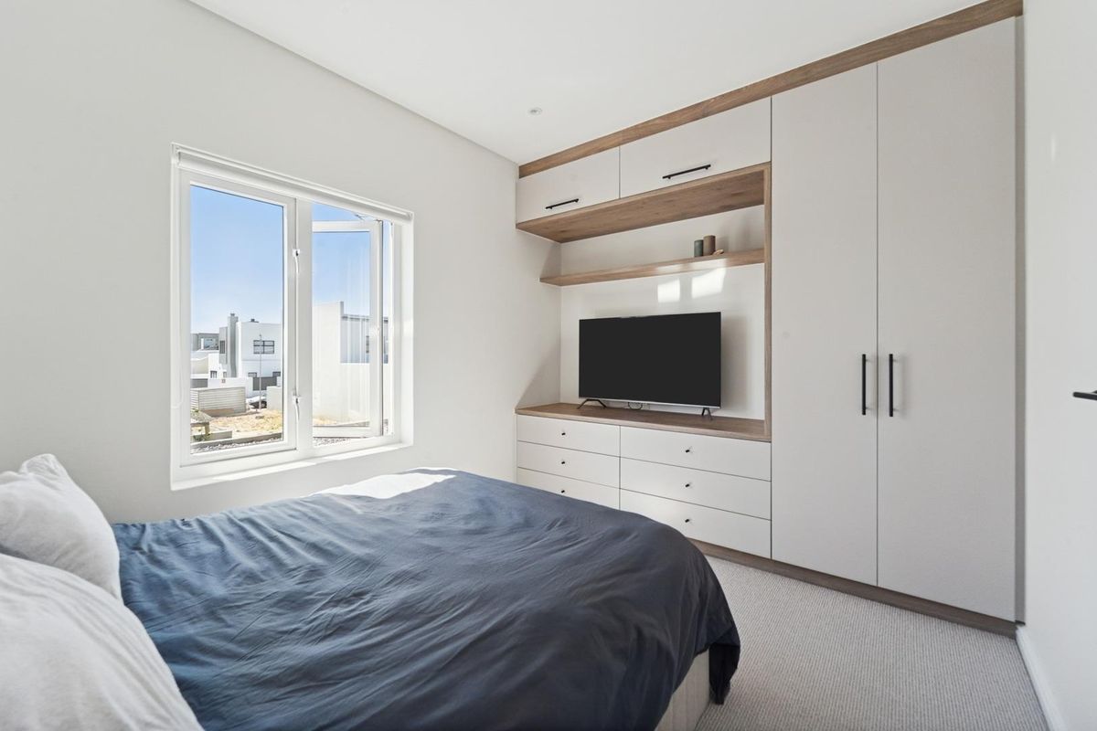 A modern bedroom featuring built-in cabinetry with integrated shelving and storage, neutral carpeting, and a window providing natural light.