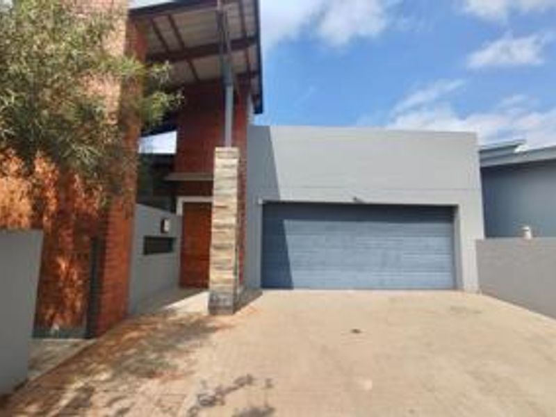 Modern townhouse exterior featuring a double garage, stone-clad pillar, and striking exposed brick facade with a covered entrance.