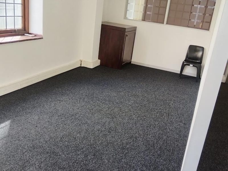 A vacant office space featuring dark carpeting, a leaded glass window, and an internal glass partition wall.