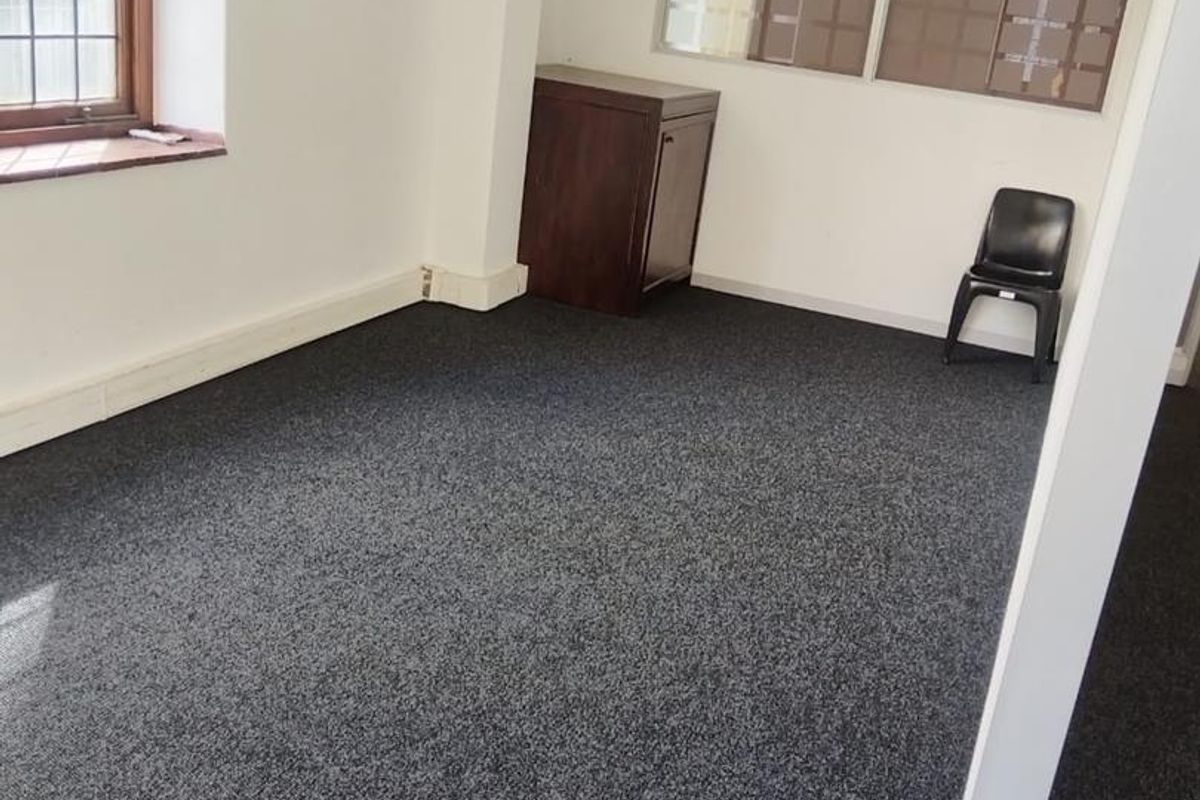 A vacant office space featuring dark carpeting, a leaded glass window, and an internal glass partition wall.