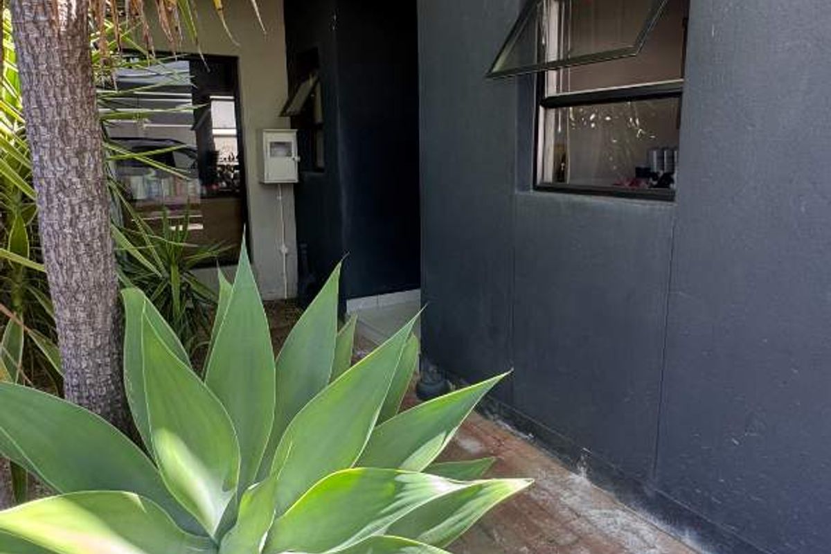 A side exterior view of the property featuring dark painted exterior walls, brick paving, and established garden landscaping.
