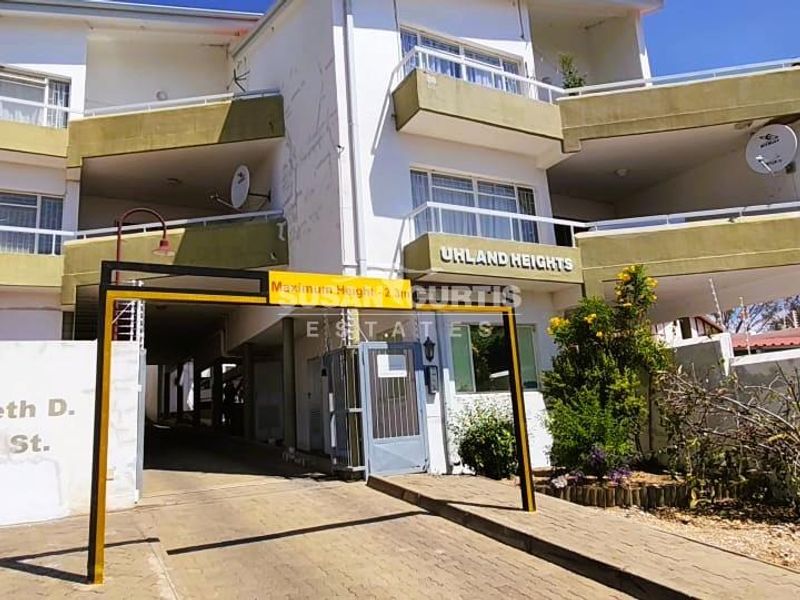 Front elevation of Uhland Heights apartment complex featuring a gated driveway entrance, multi-level balconies, and visible exterior wall maintenance requirements.