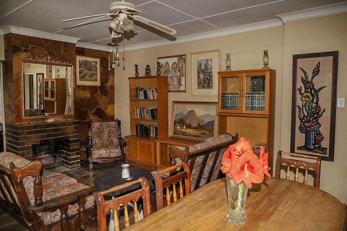 A living room featuring a prominent stone fireplace with a brick hearth, coved ceilings, and a ceiling fan, showcasing dated interior finishes.