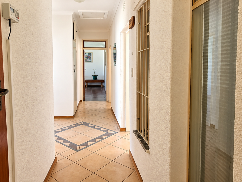 A bright, tiled hallway featuring a security gate and access to multiple rooms, providing a clean and functional transition space within the home.