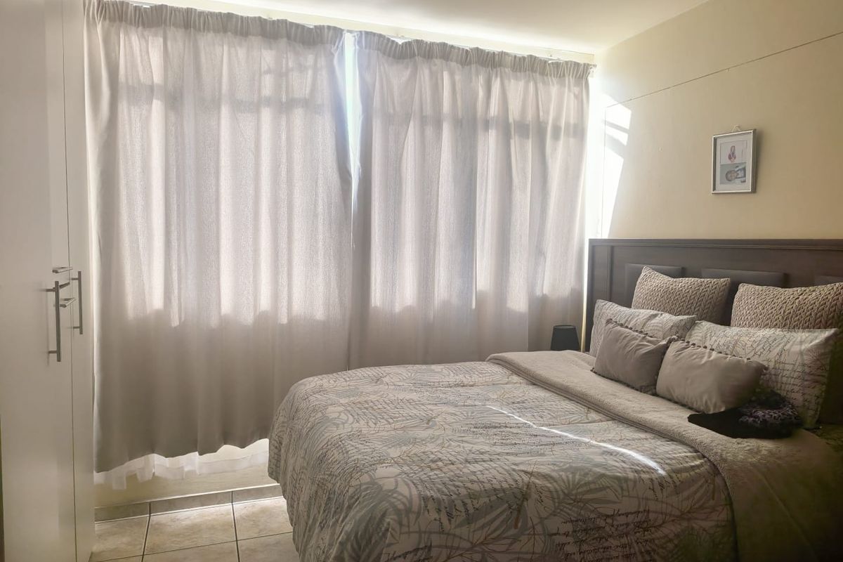 A bedroom featuring tiled flooring and built-in white cabinetry, illuminated by natural light through large window curtains.