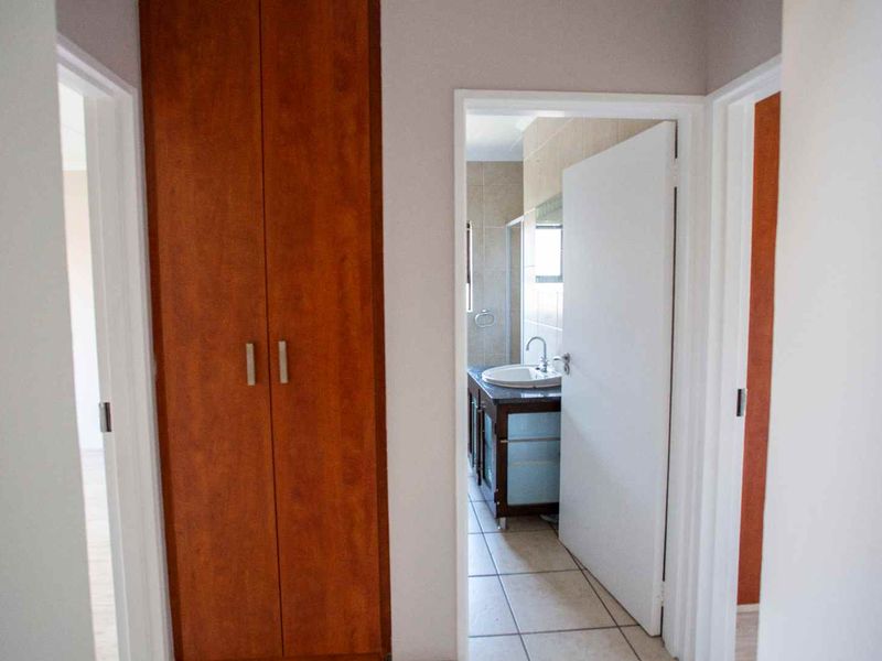 A functional hallway featuring built-in wooden cupboards and tiled flooring, providing access to adjacent rooms including a bathroom.