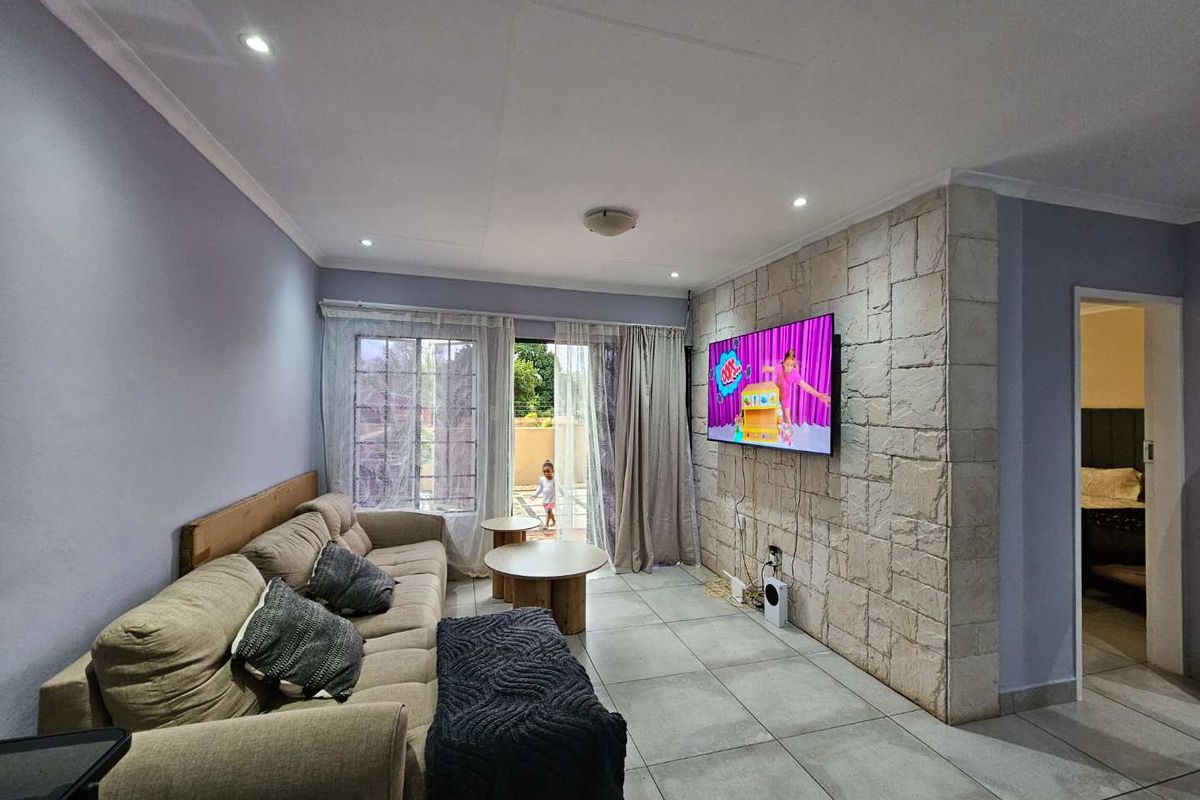 A comfortable living room featuring a textured stone accent wall, large format floor tiles, and sliding glass doors providing access to the patio.