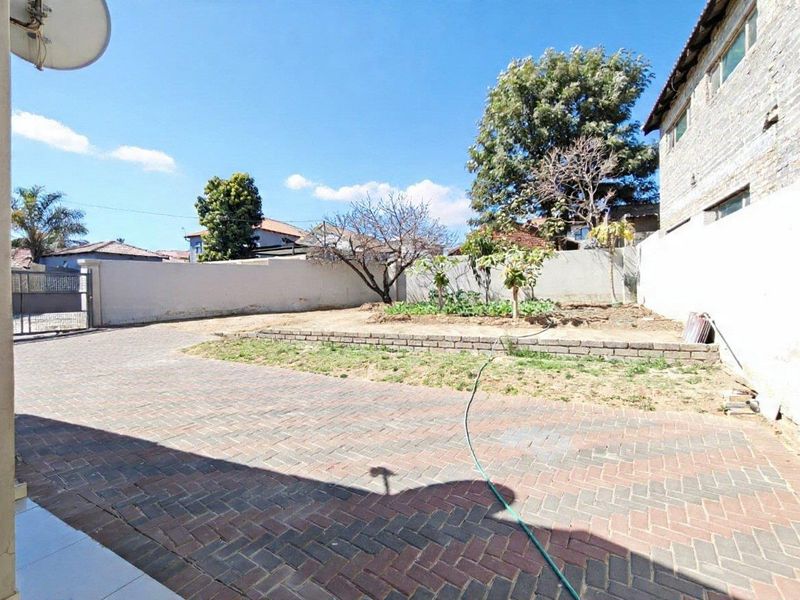 A spacious rear yard featuring extensive brick paving, a raised garden bed, and perimeter boundary walls.