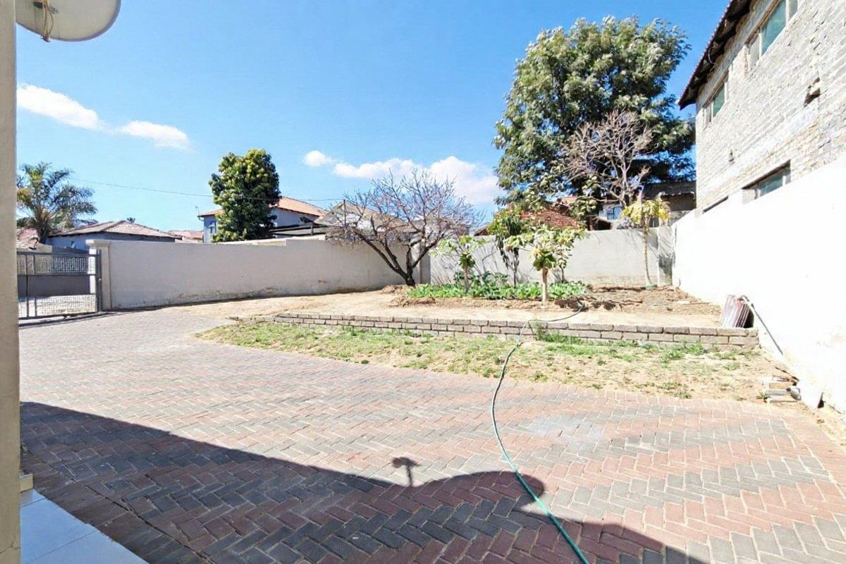 A spacious rear yard featuring extensive brick paving, a raised garden bed, and perimeter boundary walls.