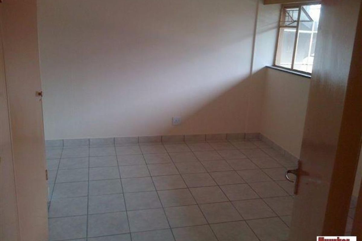 A simple, empty bedroom featuring tiled flooring and a window, providing a blank canvas for personalization.