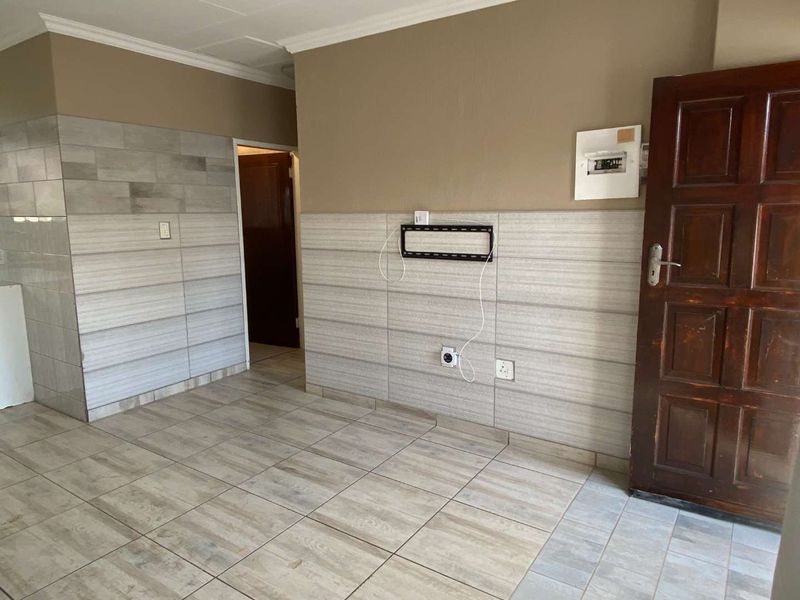An empty living area featuring tiled flooring, partial wall tiling, and a timber entrance door, providing a neutral base for interior design.