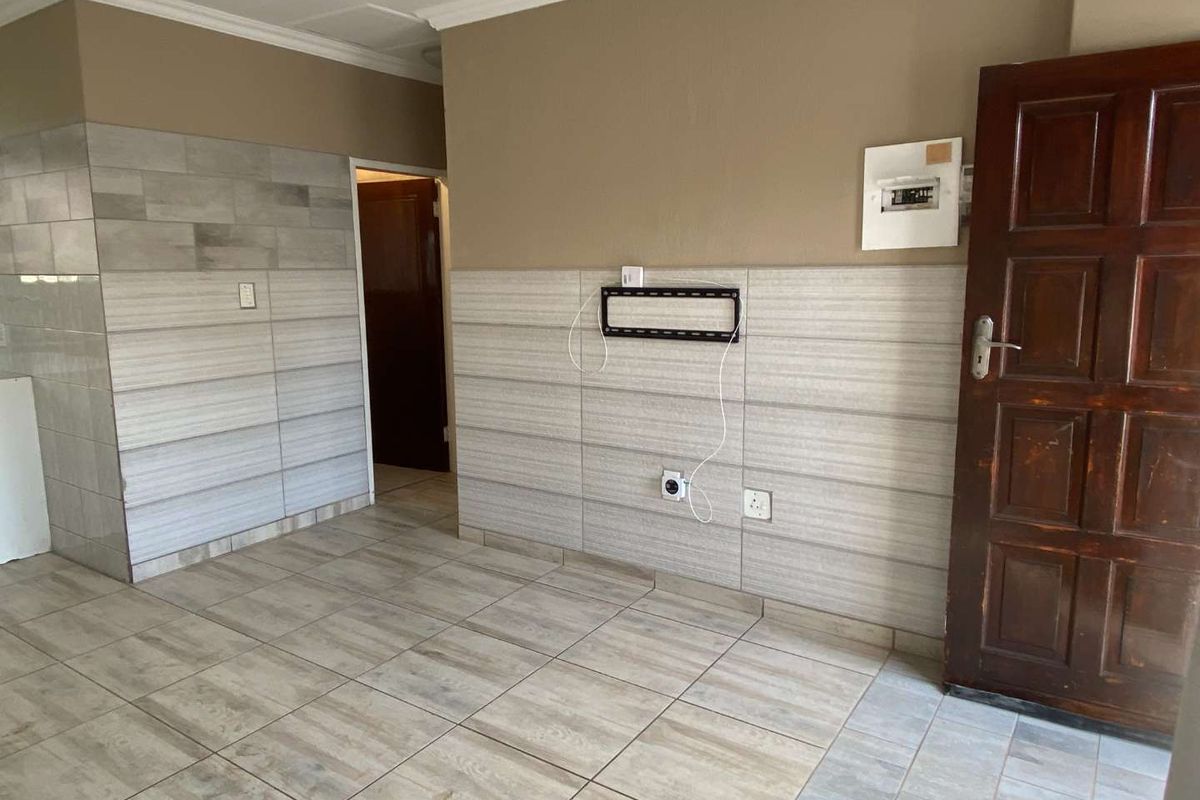 An empty living area featuring tiled flooring, partial wall tiling, and a timber entrance door, providing a neutral base for interior design.