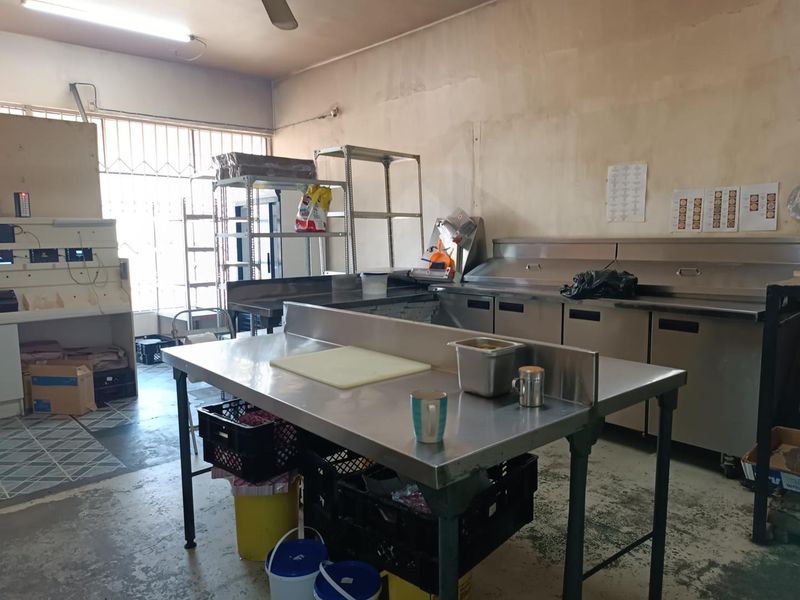 Commercial kitchen space featuring stainless steel prep tables, under-counter refrigeration units, metal shelving, and security-barred windows.