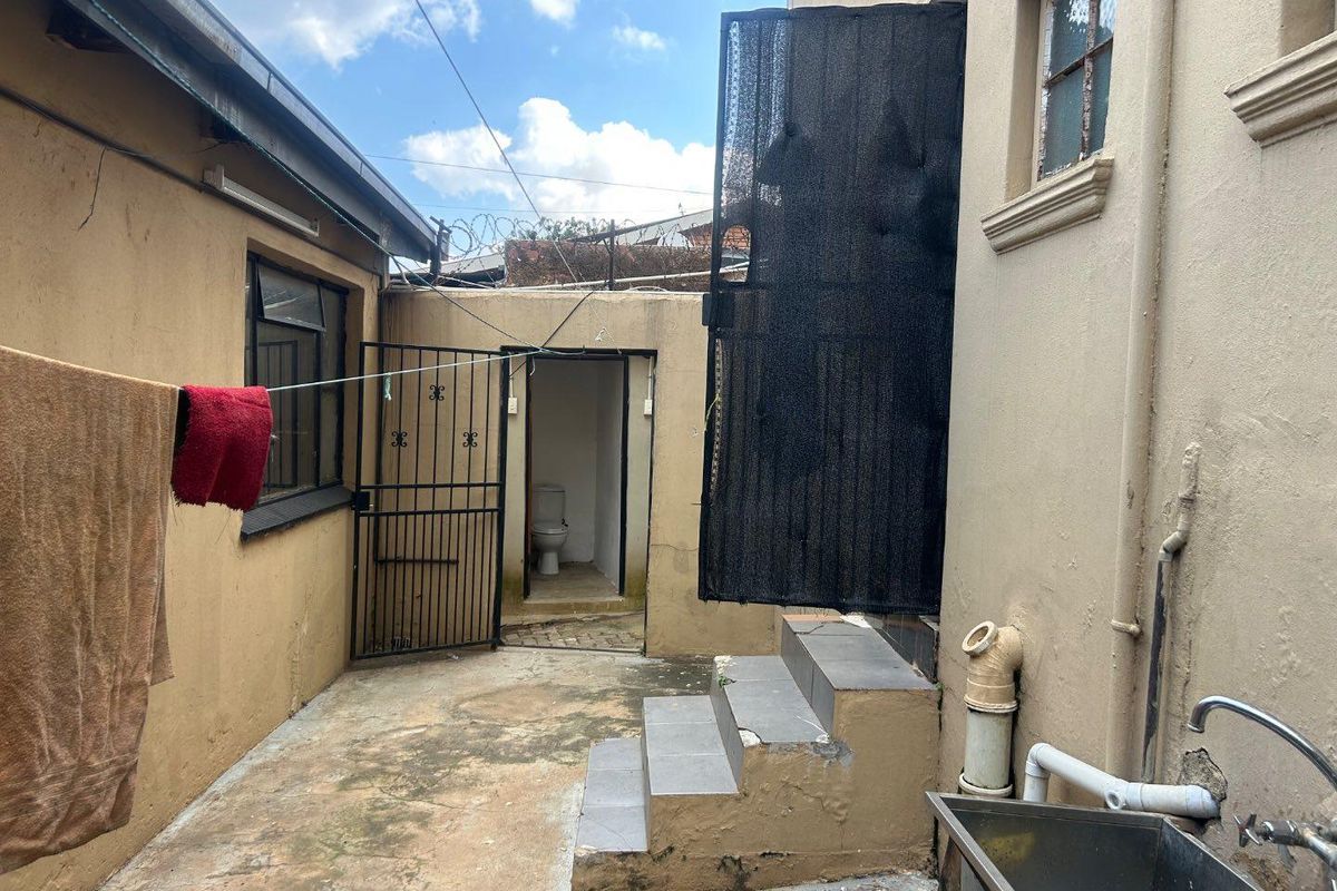 Rear courtyard area featuring a concrete patio, external utility sink, tiled steps, and access to an outdoor toilet facility.