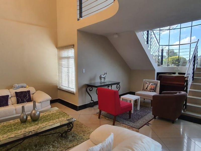 Spacious double-volume living area featuring tiled flooring, a prominent staircase with a modern stainless steel balustrade, and large windows allowing ample natural light.