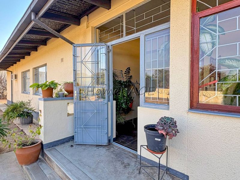 Front entrance area featuring a security gate, concrete steps, and metal-framed windows with a textured exterior wall finish.