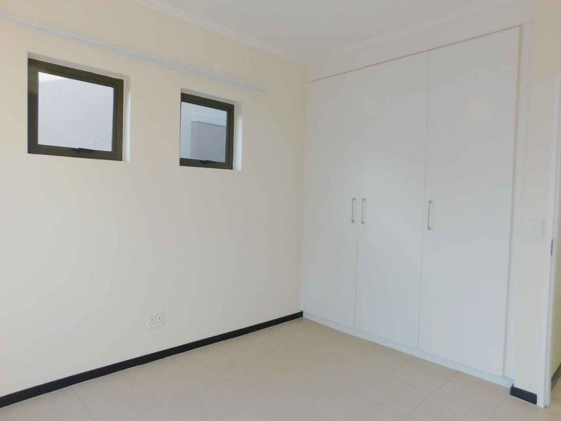 A clean, empty bedroom featuring neutral tiled flooring, built-in white cupboards, and two small casement windows.