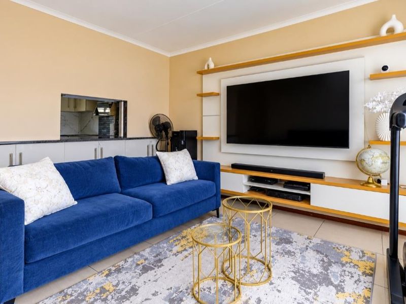 A well-maintained living room featuring a custom built-in media wall unit, tiled flooring, and a convenient serving hatch connecting to the kitchen area.