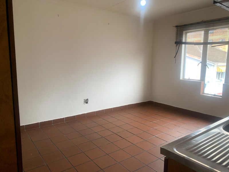 An empty kitchen area featuring tiled flooring, a stainless steel sink, and a window with a blind, ready for renovation or customization.