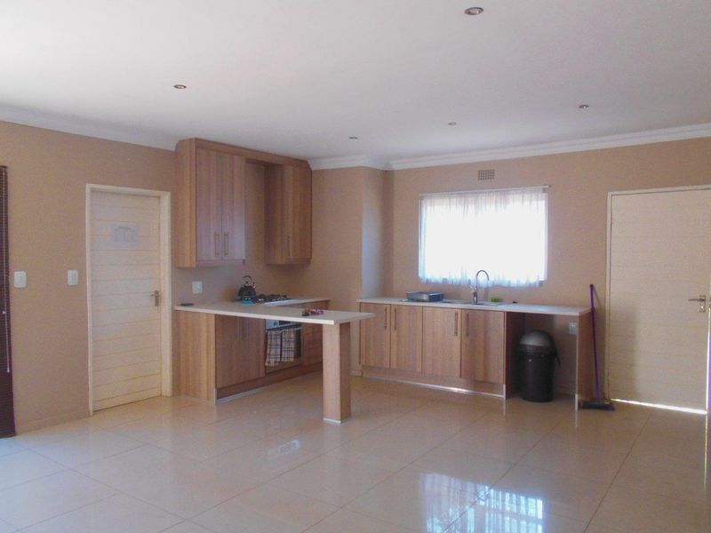 A spacious, open-plan kitchen featuring light wood-finish cabinetry, laminate countertops, integrated appliances, and neutral tiled flooring, offering a clean and functional layout.
