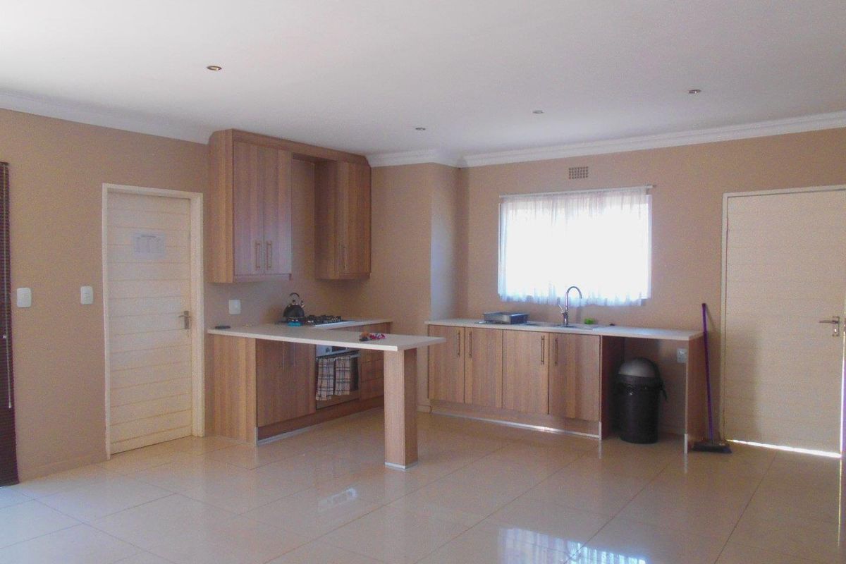 A spacious, open-plan kitchen featuring light wood-finish cabinetry, laminate countertops, integrated appliances, and neutral tiled flooring, offering a clean and functional layout.