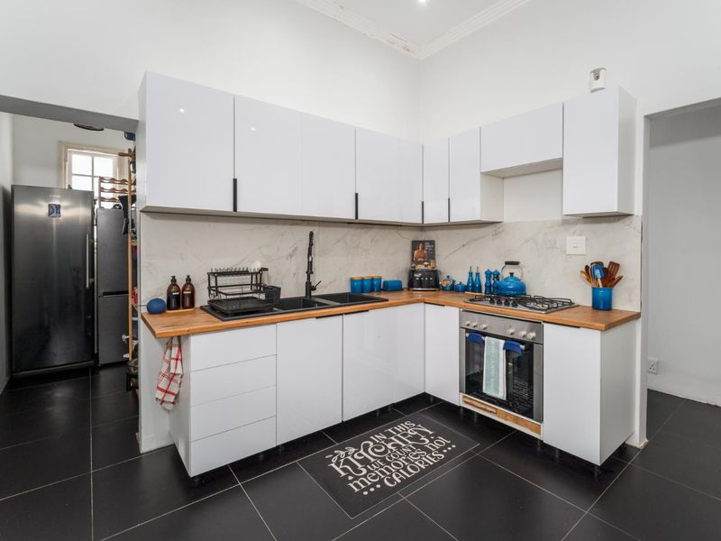 Modern kitchen featuring white gloss cabinetry, wooden countertops, built-in oven, gas hob, and marble-look splashback, complemented by dark floor tiles.