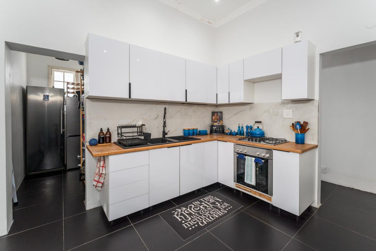 Modern kitchen featuring white gloss cabinetry, wooden countertops, built-in oven, gas hob, and marble-look splashback, complemented by dark floor tiles.