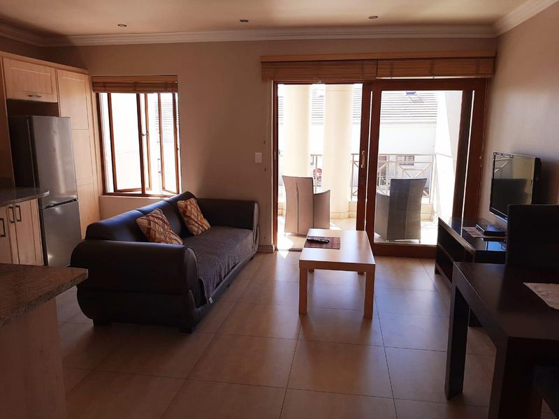 Open-plan living area featuring tiled floors, kitchen cabinetry with granite countertops, and sliding glass doors leading to a balcony.
