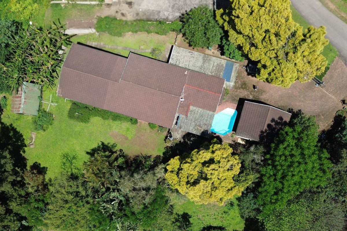 Aerial view of a residential property featuring a tiled roof, a swimming pool, and extensive surrounding garden space with mature trees.
