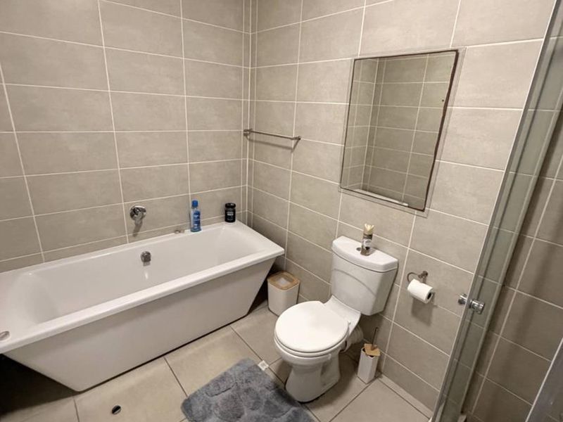 A modern bathroom featuring neutral wall and floor tiles, a bathtub, a separate shower enclosure, and a wall-mounted mirror.