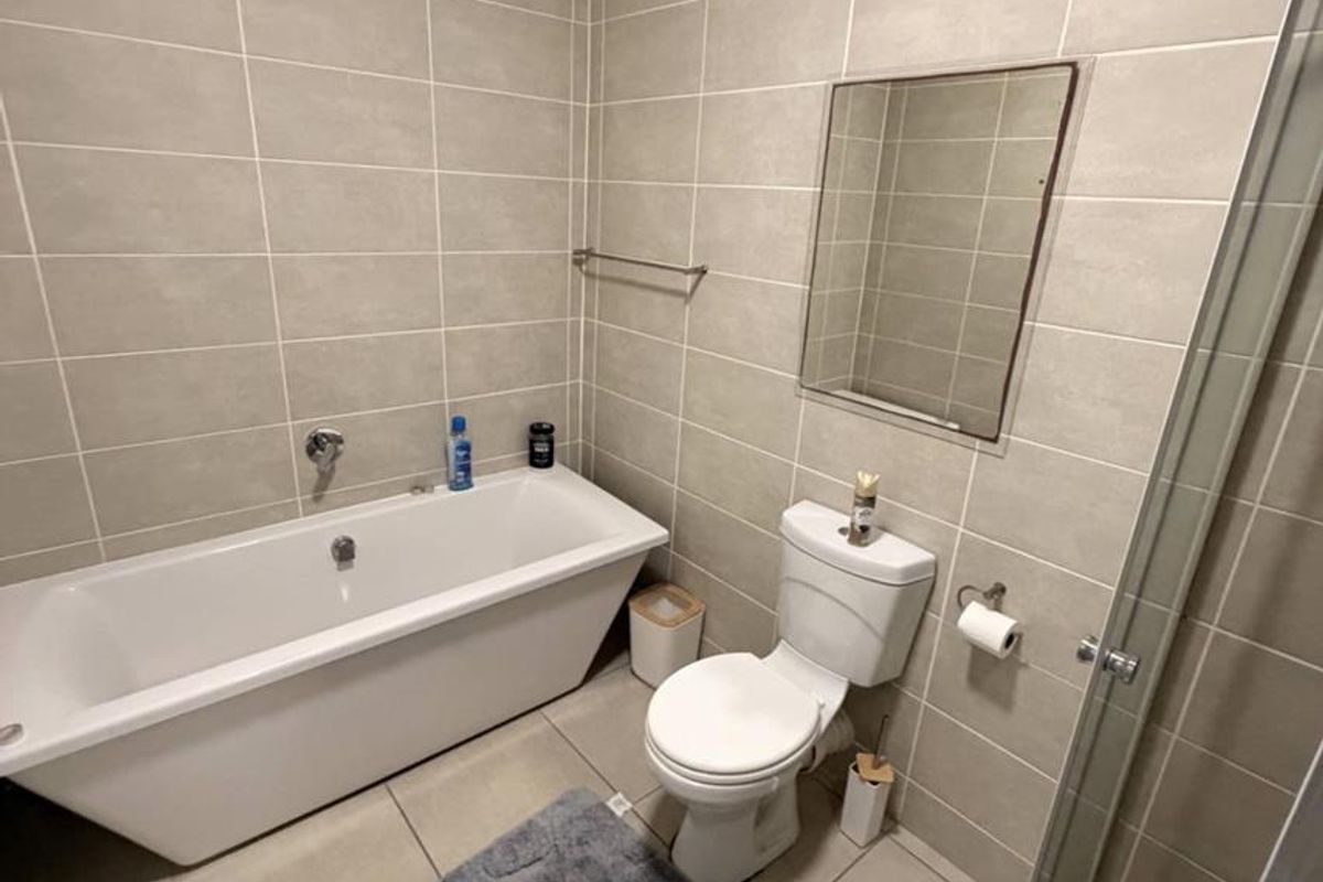 A modern bathroom featuring neutral wall and floor tiles, a bathtub, a separate shower enclosure, and a wall-mounted mirror.