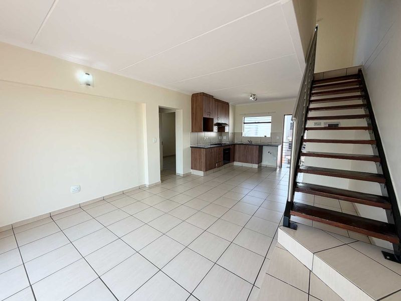 Spacious open-plan living area featuring tiled flooring, a functional kitchen with built-in cabinetry and appliances, and a staircase leading to the upper level.