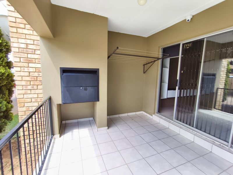 A covered balcony featuring tiled flooring, a built-in braai, a wall-mounted drying rack, and secure sliding glass door access to the interior.