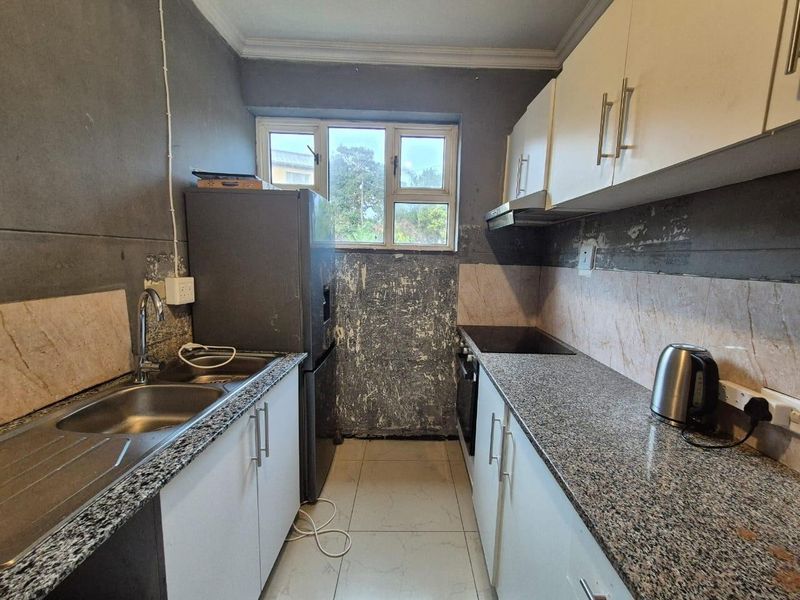 Compact kitchen featuring granite countertops, built-in oven, hob, and extractor fan, currently requiring wall surface repairs and cosmetic updates.