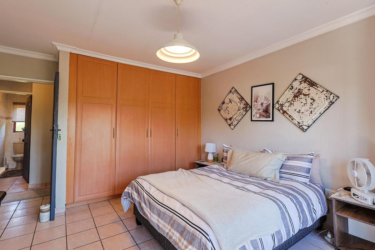 A bedroom featuring built-in wooden cupboards, tiled flooring, and a pendant light fixture, with an adjoining view into a bathroom.