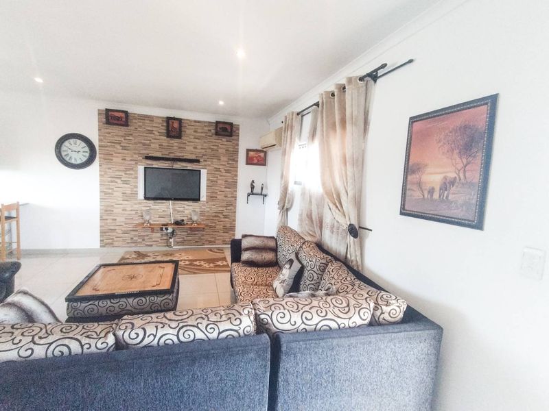 A living room featuring a stone-cladding accent wall, tiled flooring, and recessed lighting, providing a functional and comfortable space.