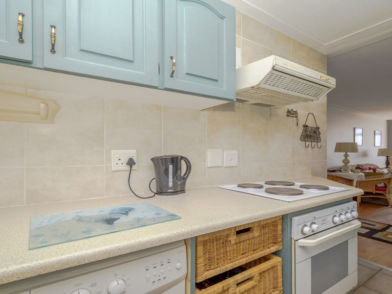 A functional kitchen featuring built-in cabinetry, an electric hob, an oven, and a tiled backsplash, opening into an adjacent living and dining area.