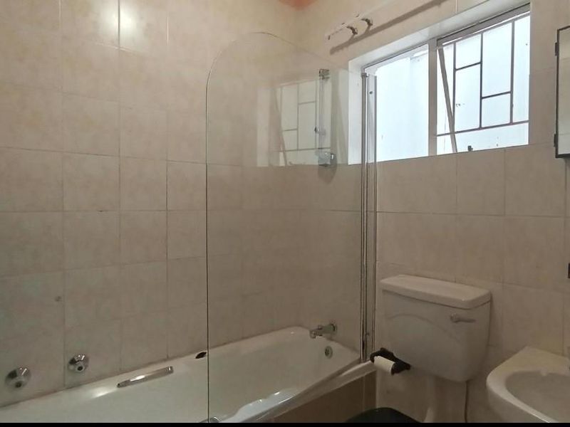 A functional bathroom featuring a bathtub with a glass screen, pedestal basin, toilet, and neutral wall tiling.