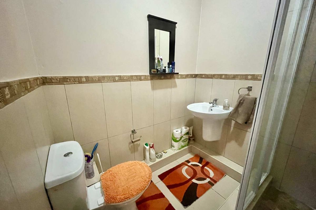 A functional bathroom featuring a pedestal sink, a standard toilet, and a shower enclosure with tiled walls and a decorative border.