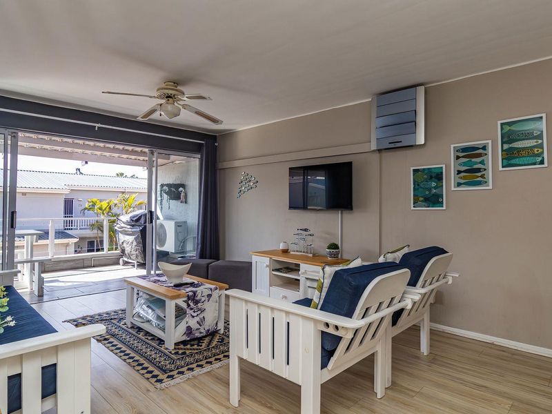 A bright living room featuring laminate flooring, a ceiling fan, and large sliding glass doors that open onto a private balcony.