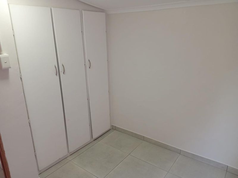 A clean, empty bedroom featuring neutral tiled flooring and white built-in cupboards, offering a blank canvas for personalization.