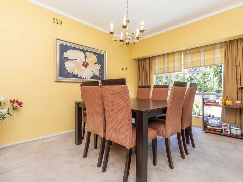 A traditional dining room featuring a central chandelier, large window with natural light, and carpeted flooring.