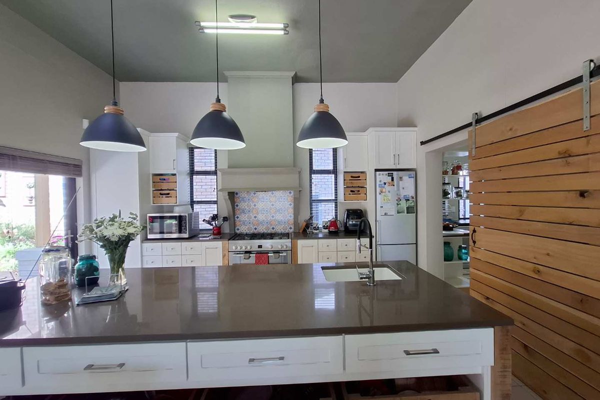 Modern kitchen featuring a large central island with stone countertop, built-in gas stove, extractor fan, and a sliding barn door leading to a scullery.