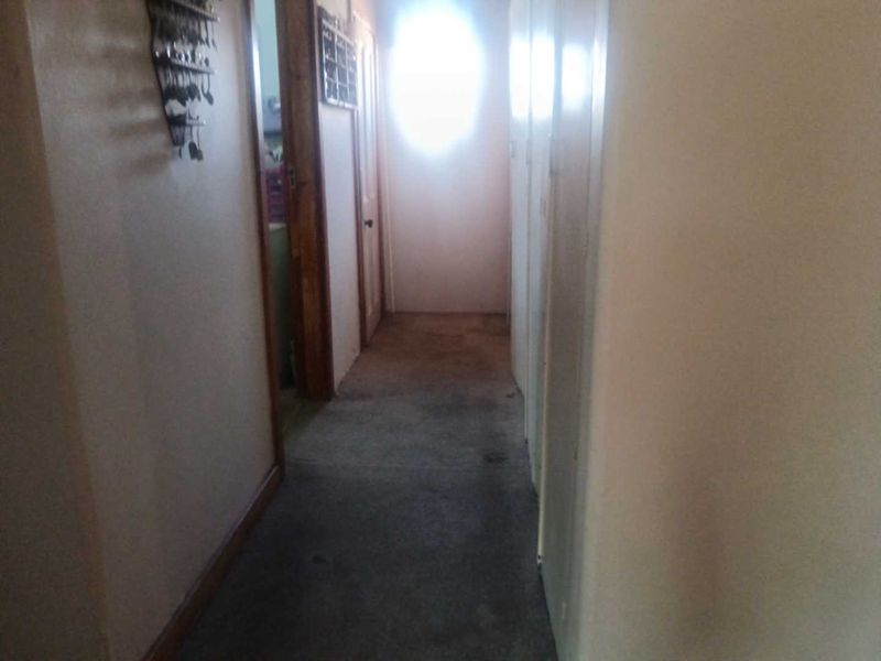 A narrow residential hallway featuring built-in storage cupboards and internal doors, currently showing signs of wear on the flooring.