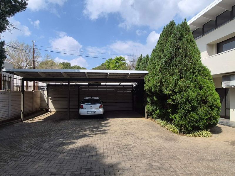 Exterior view of the office property featuring a paved driveway, covered carport, and well-maintained building facade with an external air conditioning unit.