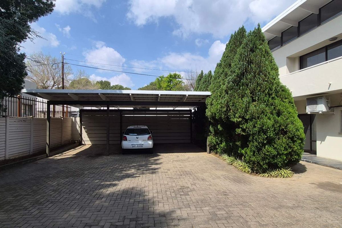 Exterior view of the office property featuring a paved driveway, covered carport, and well-maintained building facade with an external air conditioning unit.