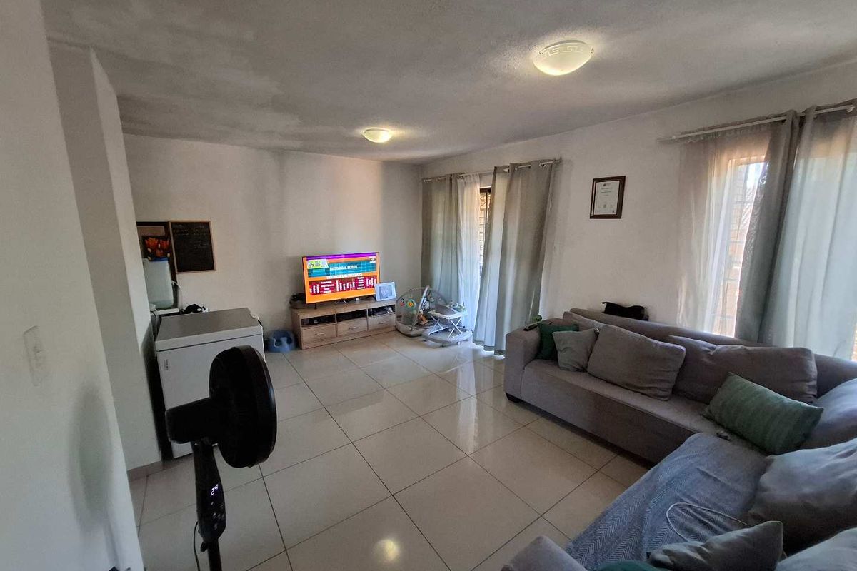 A living room featuring tiled flooring and ceiling lighting, showing visible signs of ceiling water staining requiring maintenance.