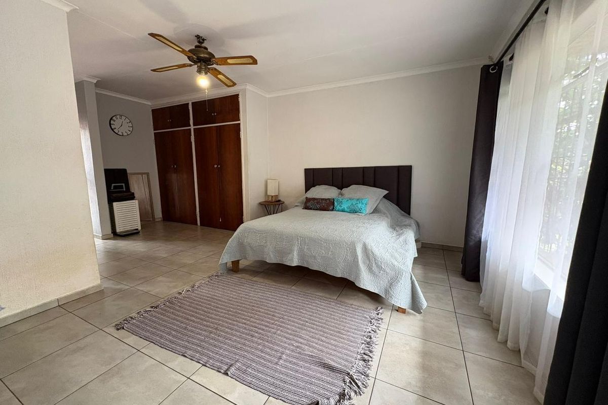 Spacious bedroom featuring tiled flooring, built-in wooden cupboards, and a ceiling fan, offering a functional and well-lit living space.